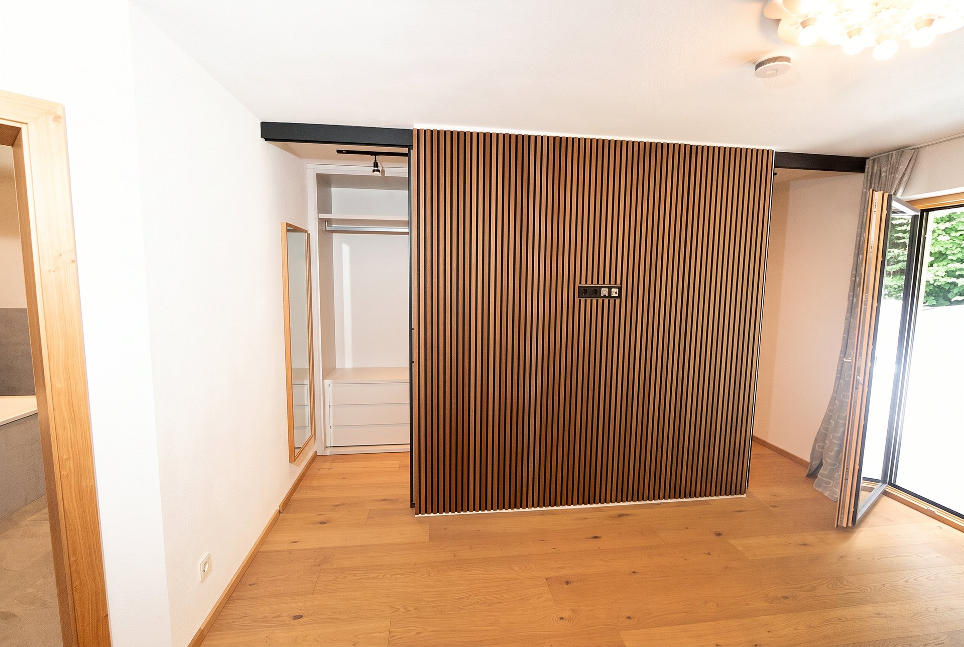 Schlafbereich mit raumhoher Eichenlamellenwand und offener Ankleide